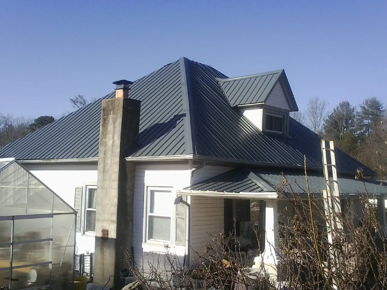 Dark blue standing seam metal roof on a white farmhouse with dormer — Slate & Tile Roof Repair by Roofing Brothers in Leonardo