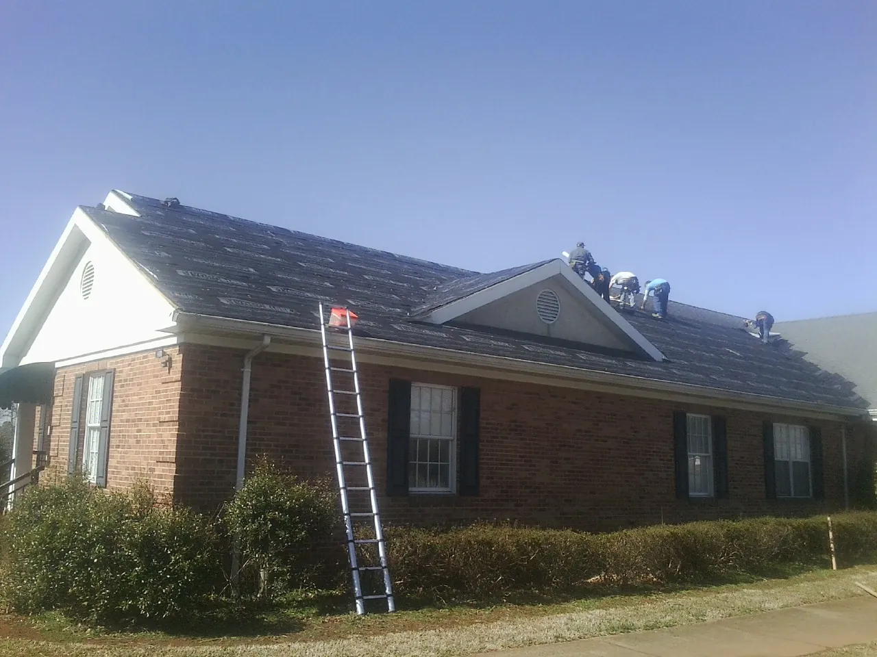 Crew tearing shingles off a brick ranch roof with a ladder set — Metal Roof Repair work by our crew in Leonardo