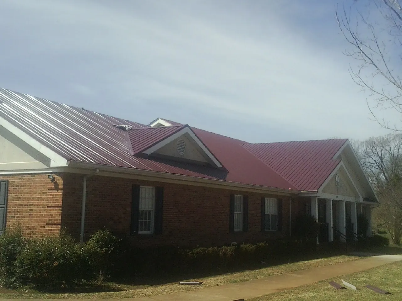 Red metal roof with gabled entries on a long brick building, from a Hail Damage Roof Repair job in Leonardo
