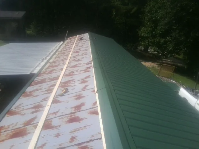Old rusted panels beside newly installed green metal roofing — Wind Damage Roof Repair by Roofing Brothers in Leonardo