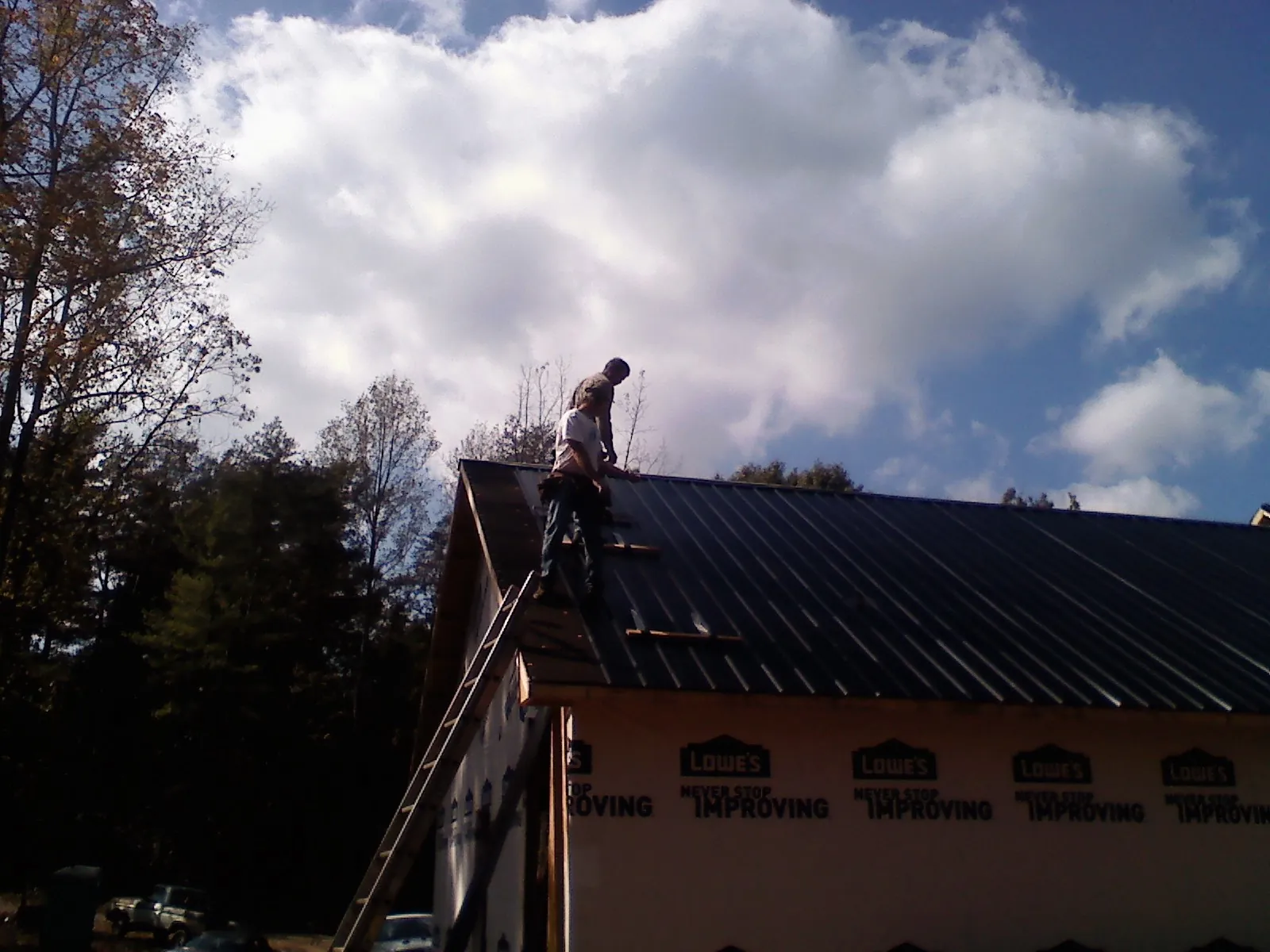 Roofer fastening dark metal panels high against a cloudy sky, from a Roof Inspection job in Leonardo
